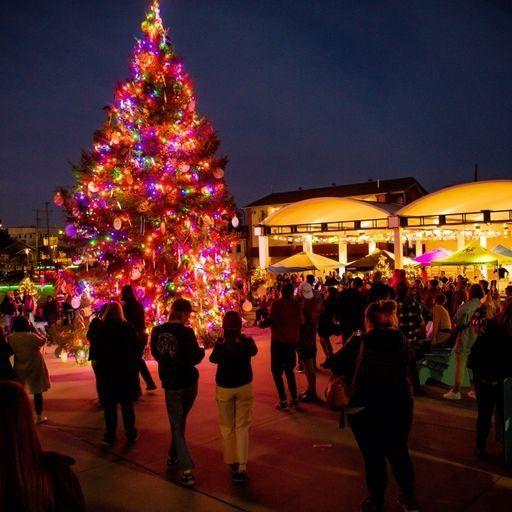 Festive street scene with a large, colorful Christmas tree at night.