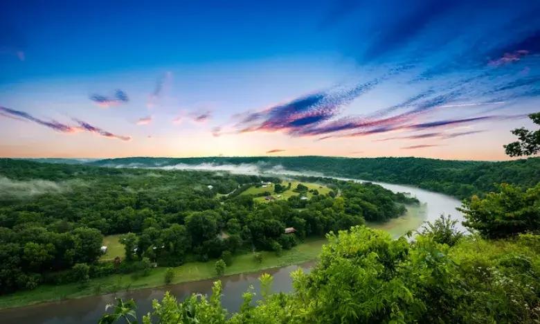 Lush green valley with a winding river under a vibrant blue and pink sunset sky.