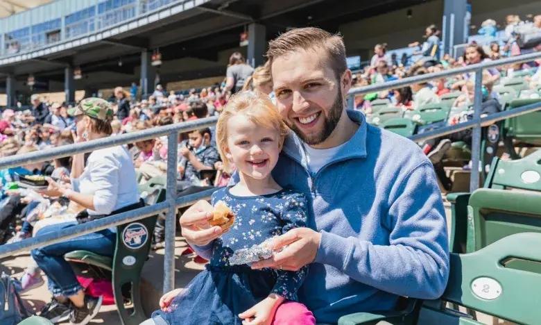 Father and daughter smiling at a crowded stadium.