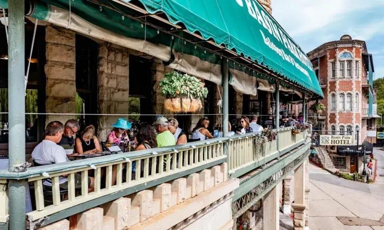 Outdoor café with people dining under a green awning on a sunny day.