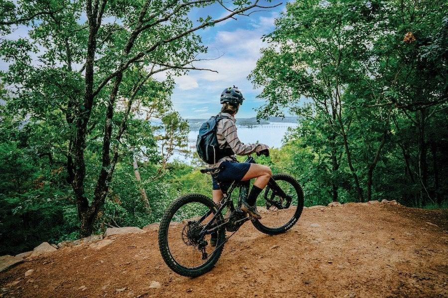 Cyclist on a dirt trail surrounded by lush green trees.