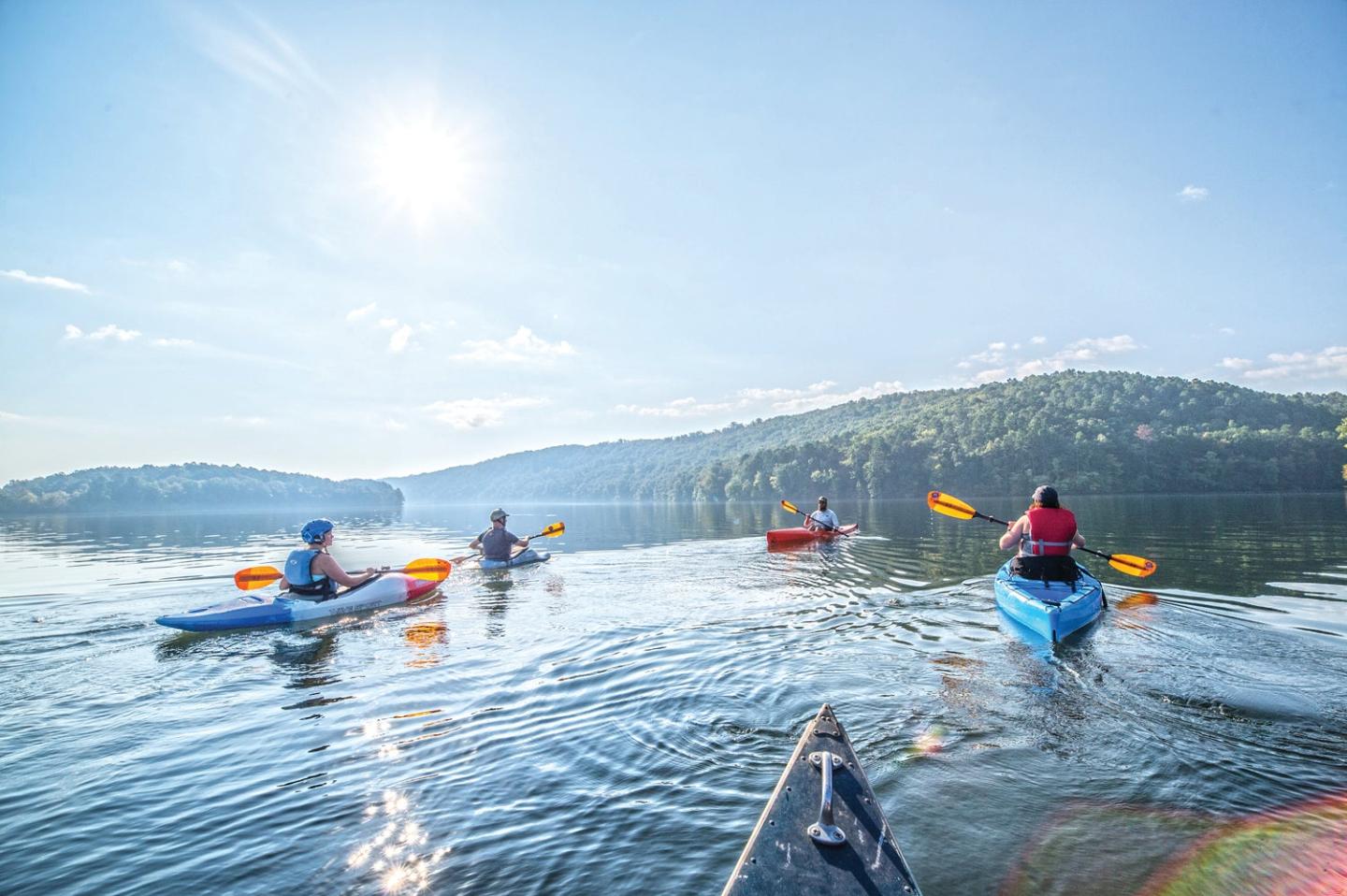 Kayakers on a sunny lake with distant hills and clear blue sky.