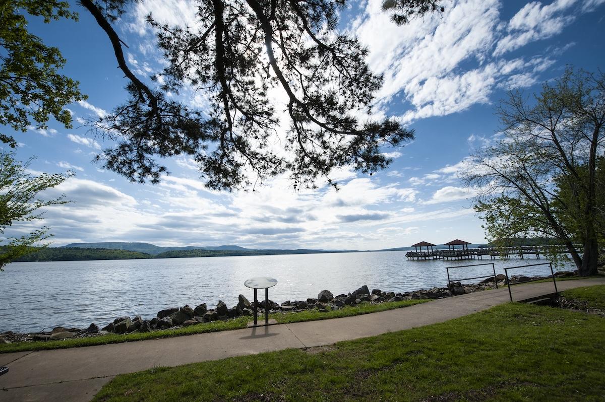 Pathway beside a lake with trees and a cloudy sky.