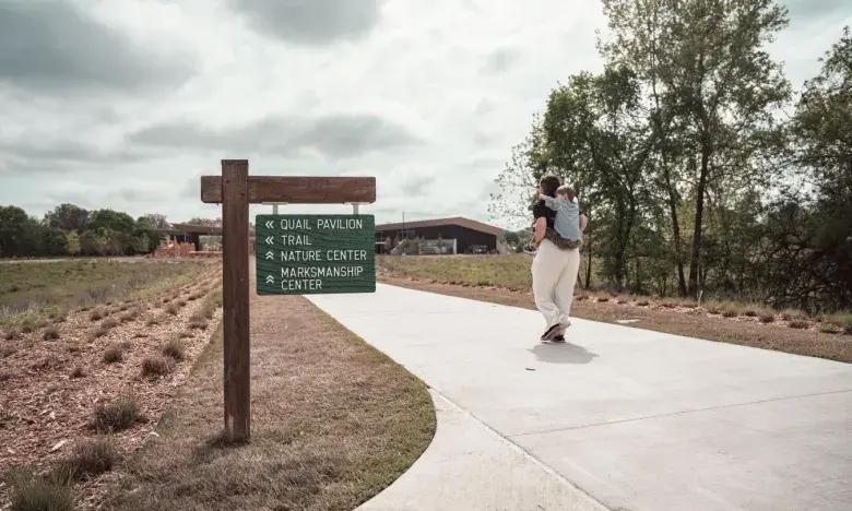 Skateboarder on a path near trees and a wooden sign in a park setting.
