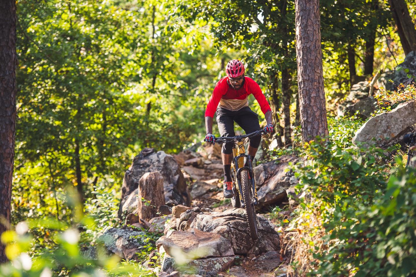 Mountain biker navigating rocky forest trail in red gear.