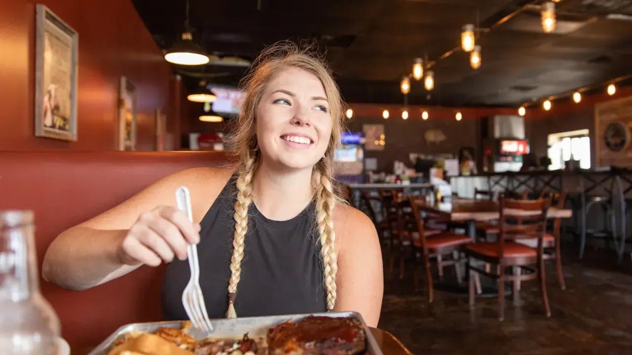 Woman with braided hair smiling in restaurant with food tray.