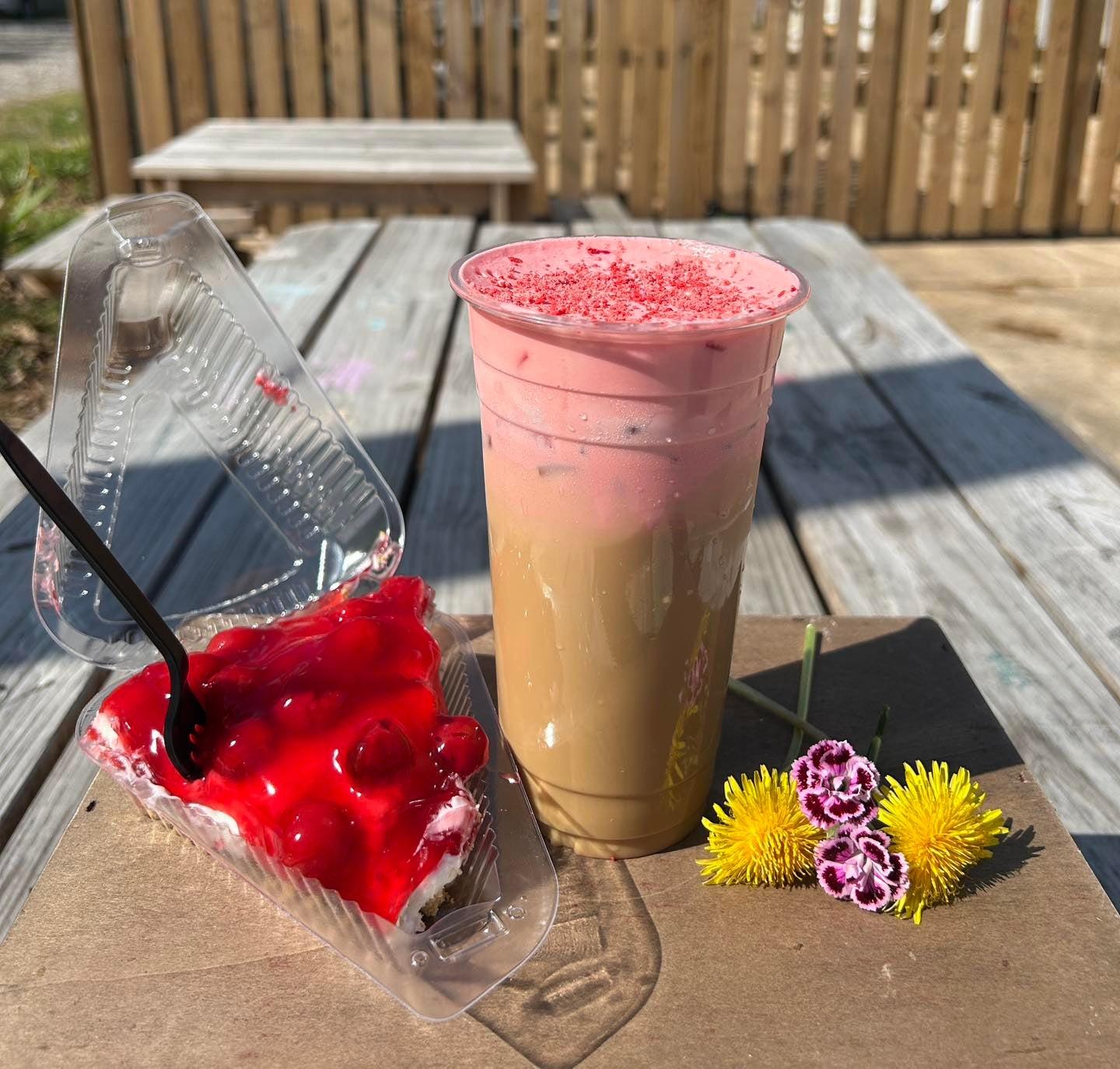 Cherry pie slice and pink-topped iced drink on a picnic table.