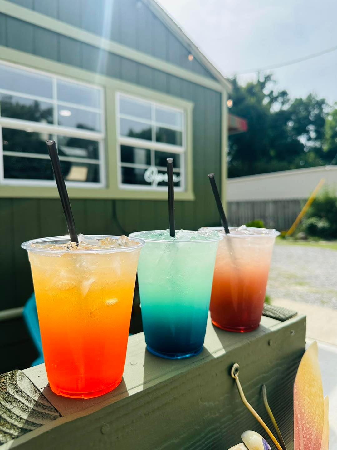 Three colorful drinks with straws on a sunny outdoor table.