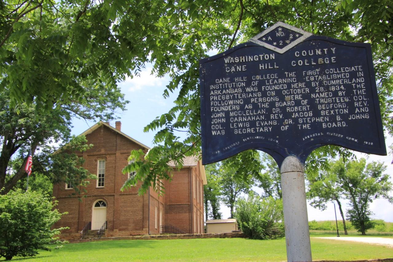 Historic brick building with a blue sign and green trees.