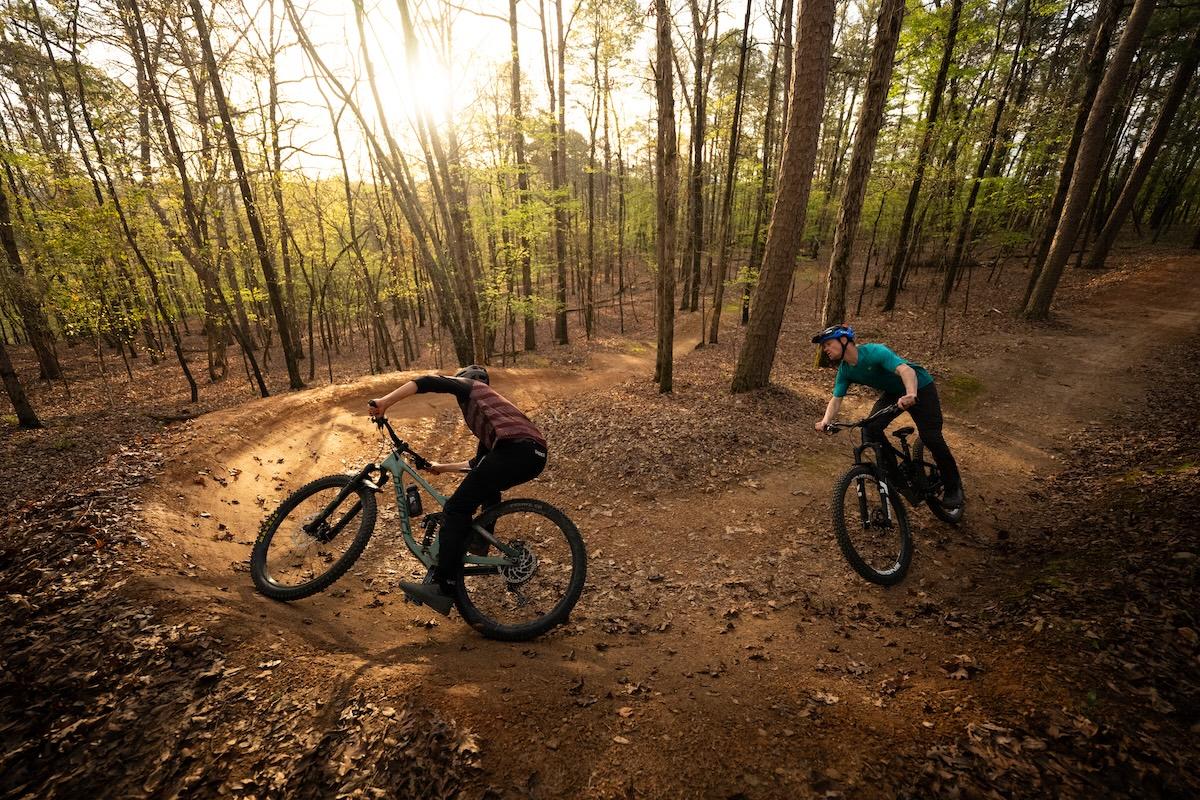 Mountain bikers navigating a forest trail at sunset.