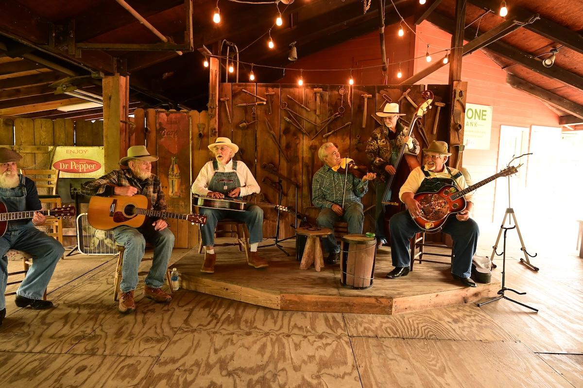 Band performing in rustic setting with string instruments and overalls.
