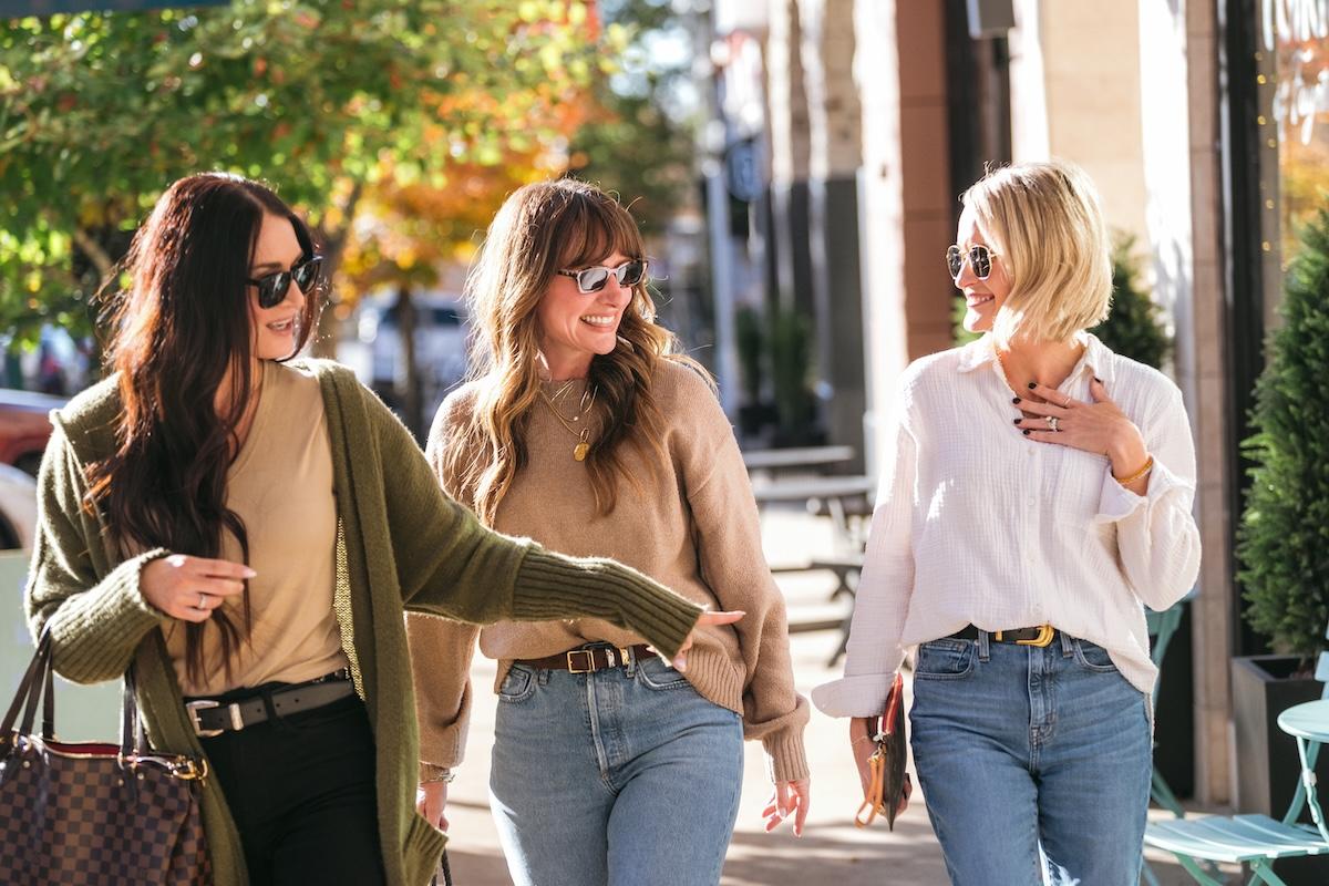 Three women walking outdoors, smiling and talking.