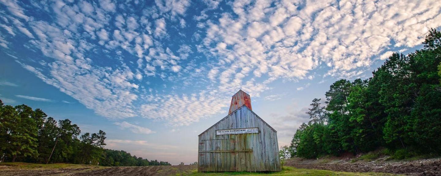 Rustic barn under a vast sky with scattered clouds, surrounded by trees and grass.