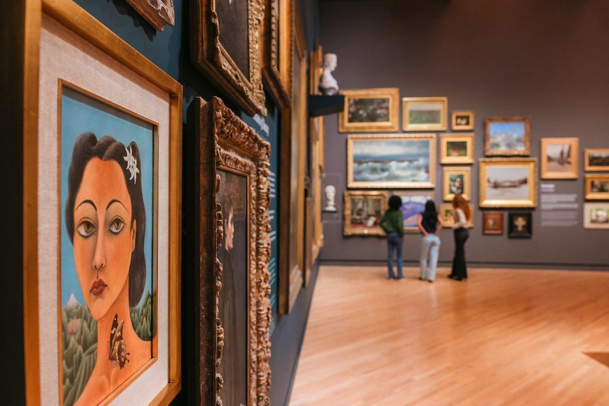 Art gallery with framed paintings and three people observing.