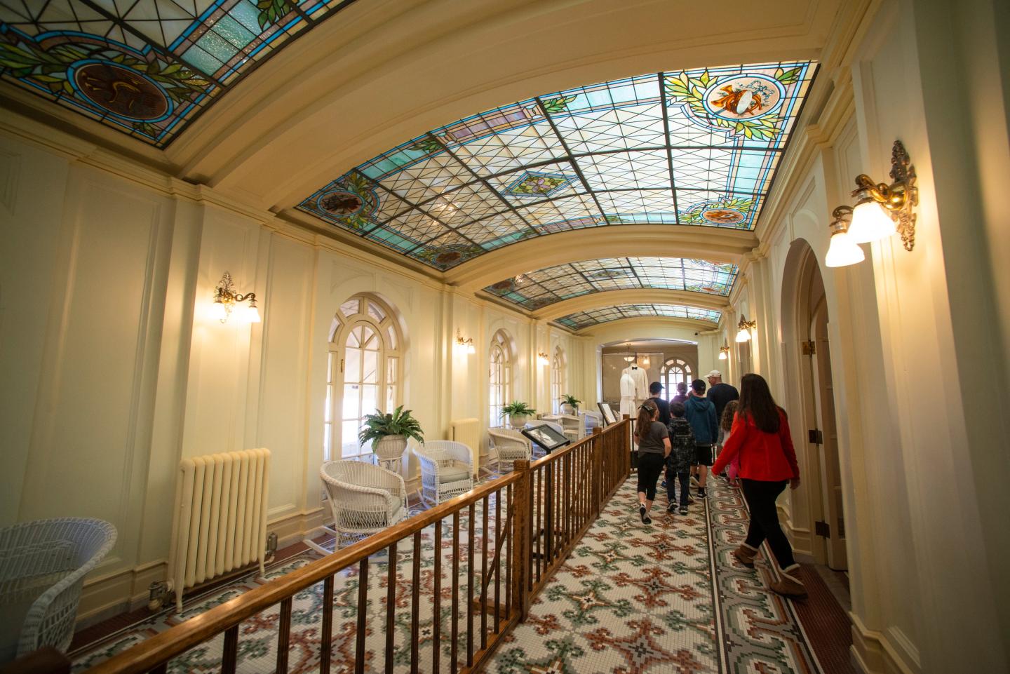 Elegant hallway with stained glass ceiling and people walking.