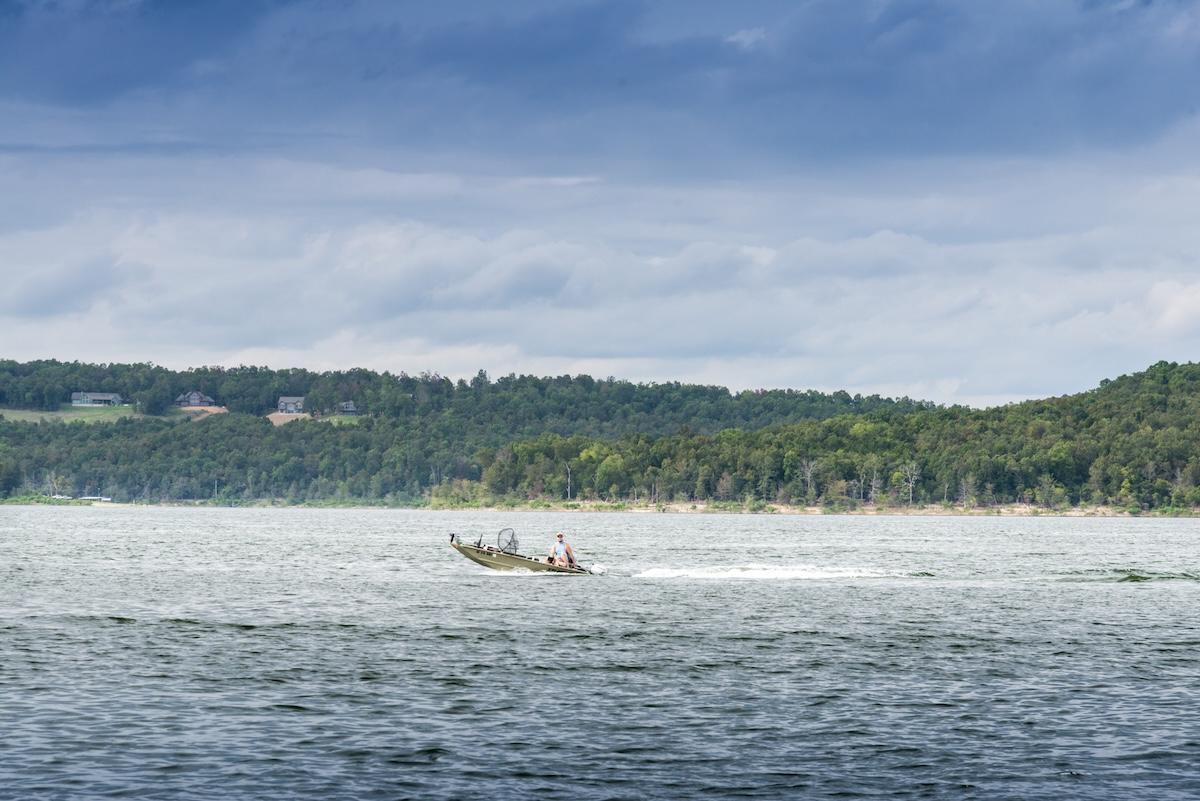 Small boat on a lake under cloudy sky near a tree-lined shore.