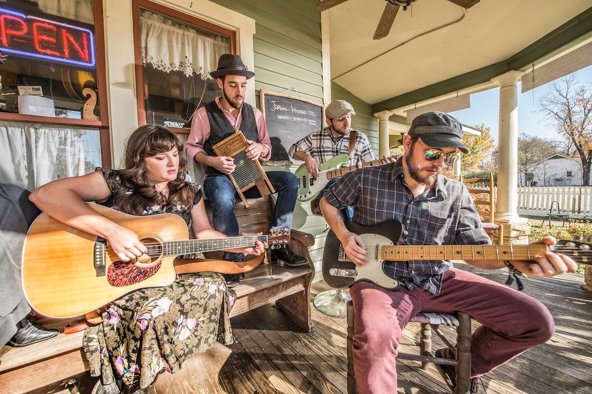 Four musicians playing guitars and a washboard on a porch.