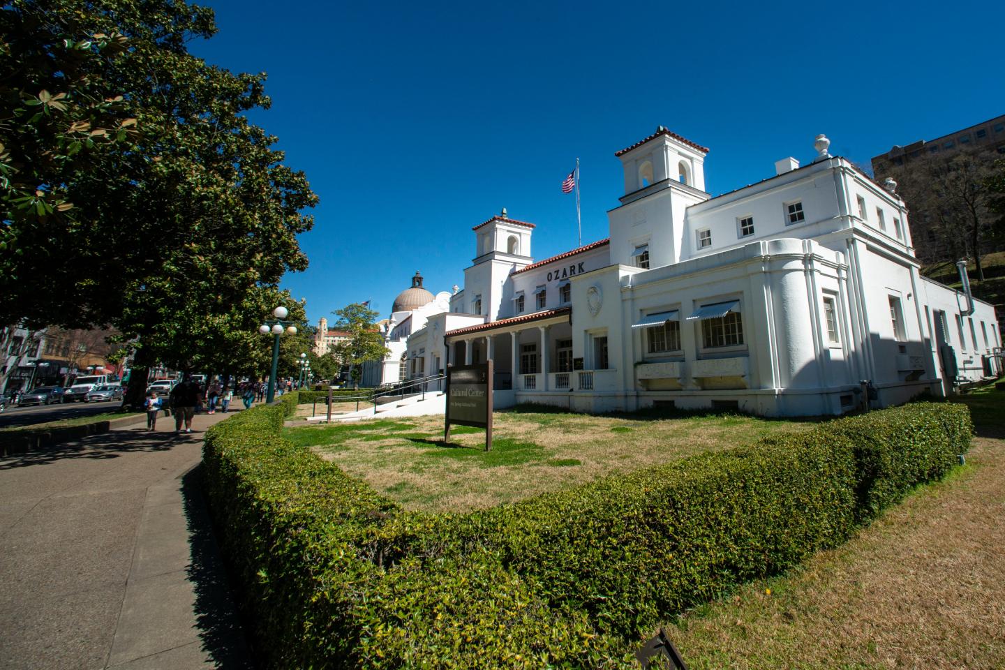 White building with turrets, surrounded by green hedges, under a clear blue sky.