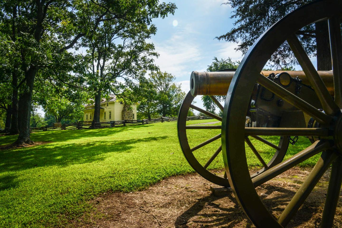 Historic cannon on a grassy field, trees and a small building in the background.