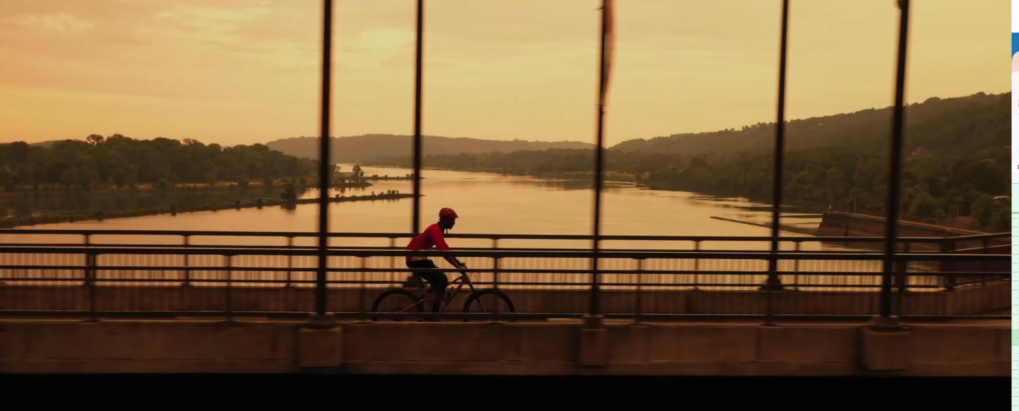Cyclist on bridge at sunset overlooking a river.