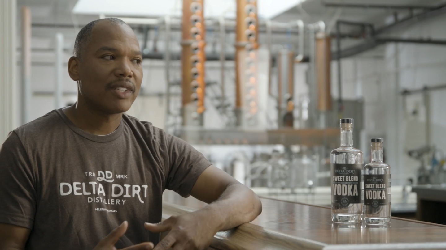 Man sitting in a distillery with bottles on the countertop.
