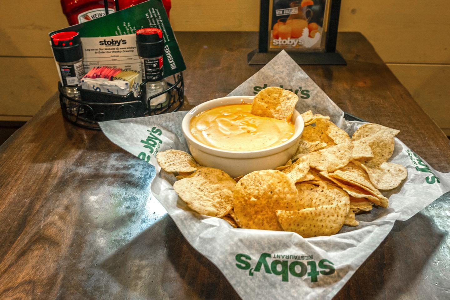 Nachos with cheese dip on a wooden table with condiments in the background.