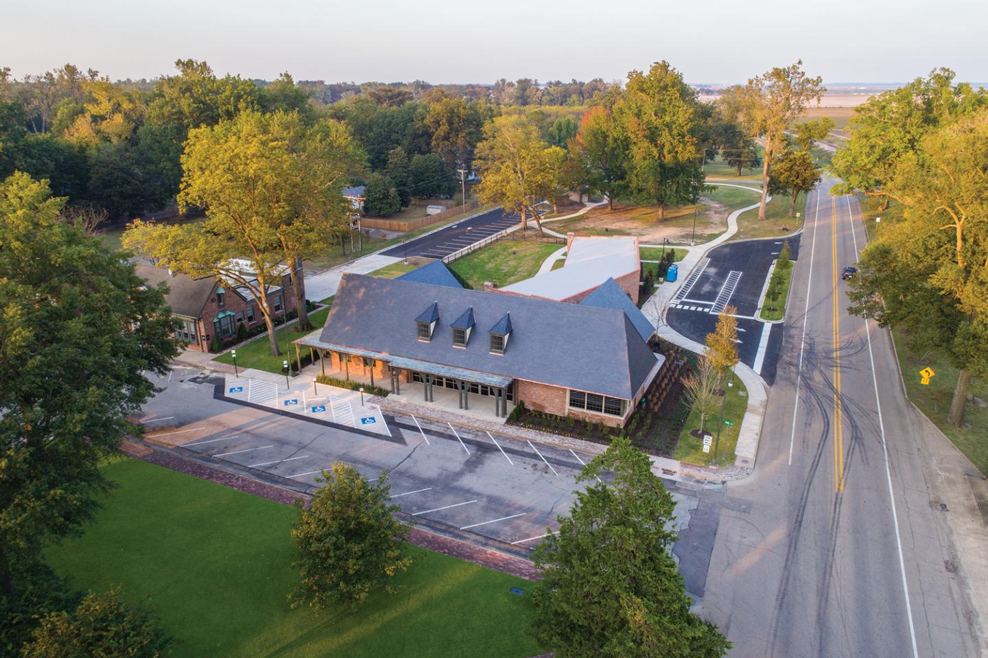 Aerial view of a two-story building with a gray roof, surrounded by trees and a road.