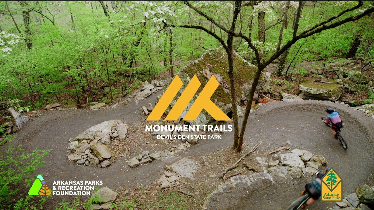 Trail through a lush forest with cyclists navigating a curved path.