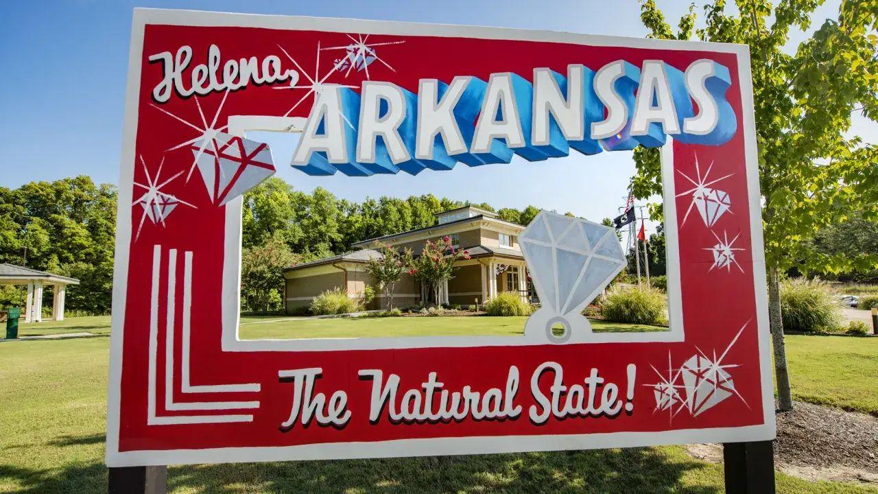 "Arkansas welcome sign with gems, greenery in background."