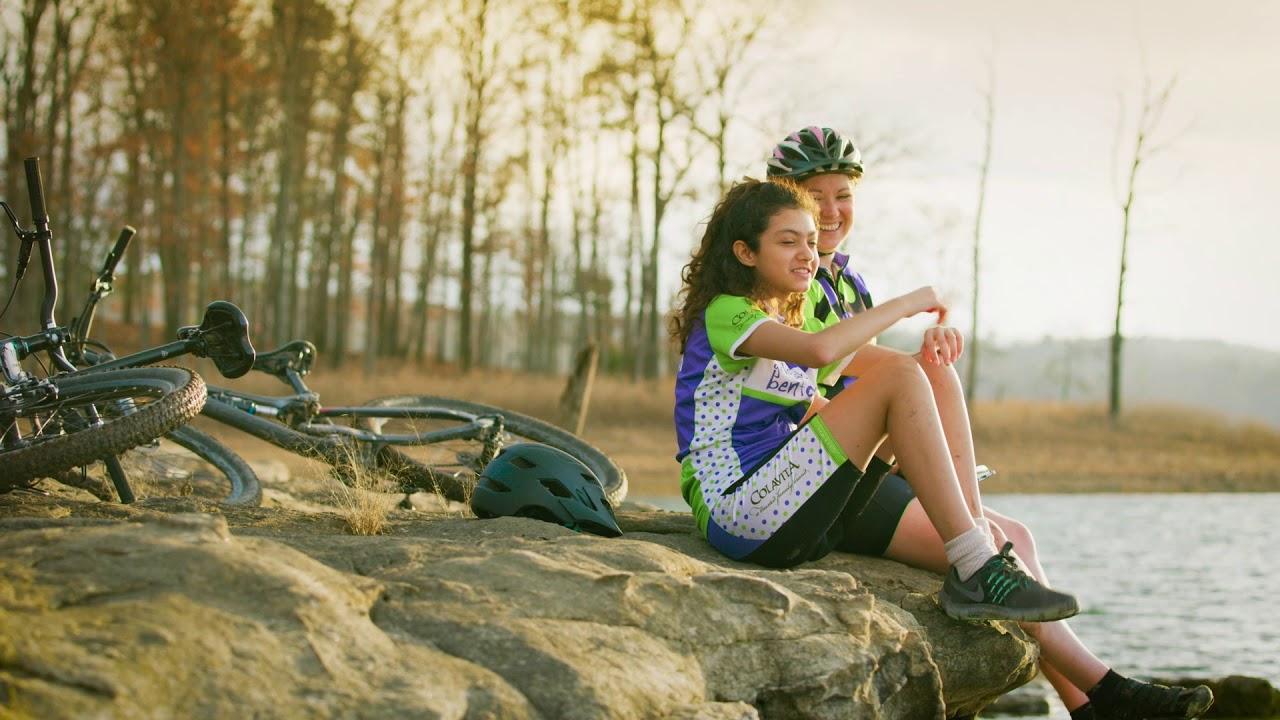 Two cyclists relaxing on rocks by a lake, with bikes nearby.