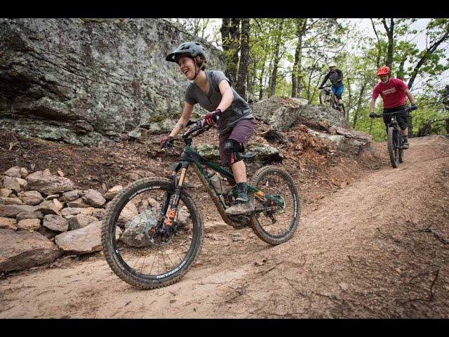 Mountain bikers ride a rocky trail in a wooded area.