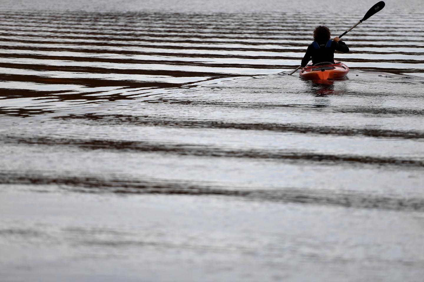 Kayaker paddling on rippled water under overcast sky.