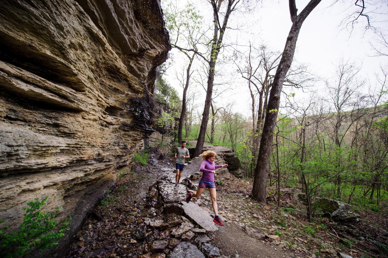 Trail runners beside a rocky cliff in a forest setting.