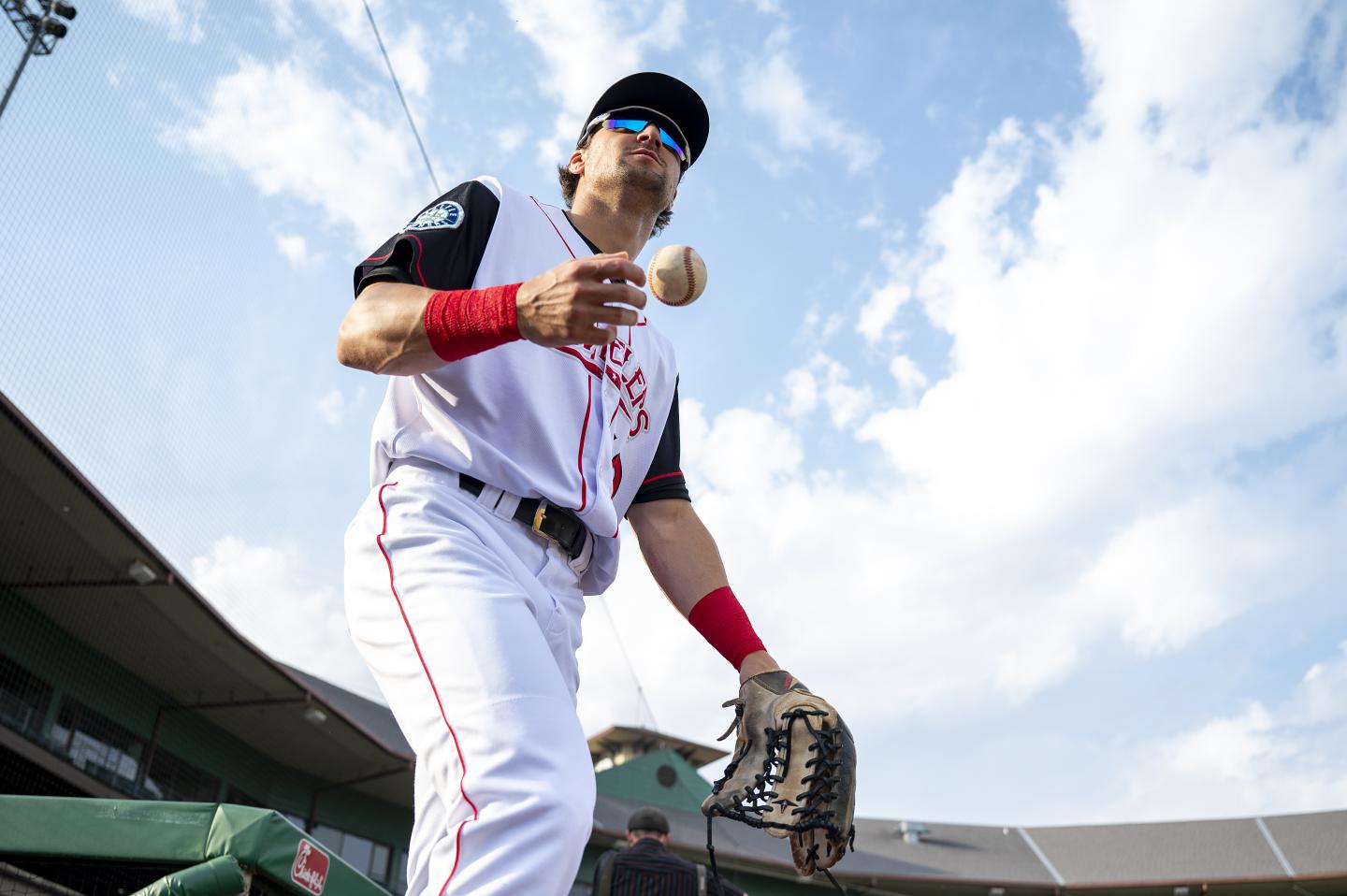 Baseball player in uniform juggling a ball on the field, sunny day.