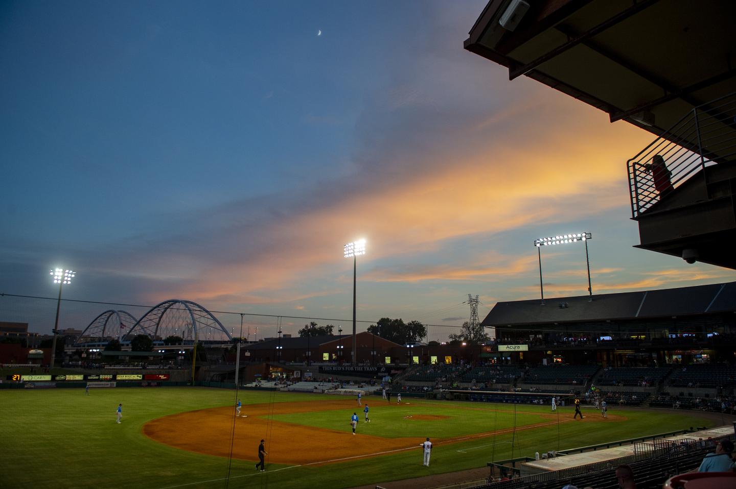 Baseball game at dusk with a vibrant sunset sky and stadium lights.