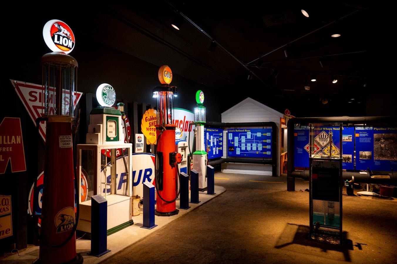Dimly lit vintage gas station exhibit with colorful signs and pumps.