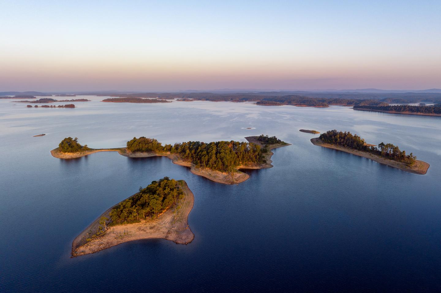Aerial view of small, tree-covered islands in a calm blue lake at sunset.