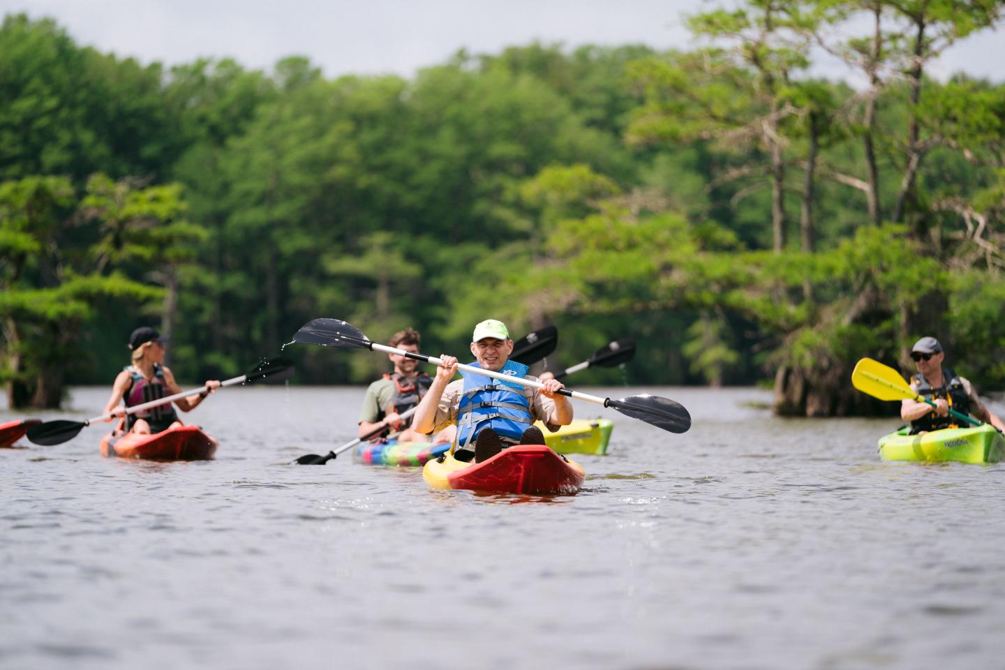 Kayakers paddling on a calm lake surrounded by trees.