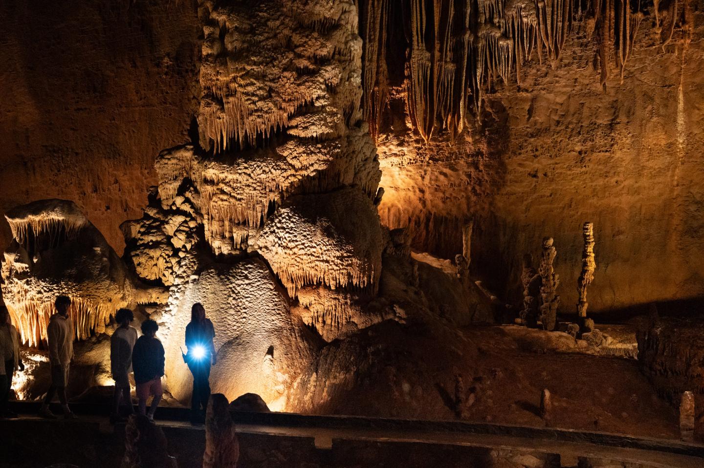 Cave interior with stalactites and people silhouetted by warm lighting.
