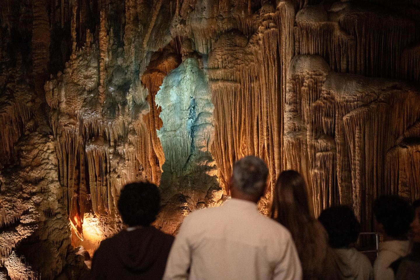 People observing stalactites in a dimly lit cavern.