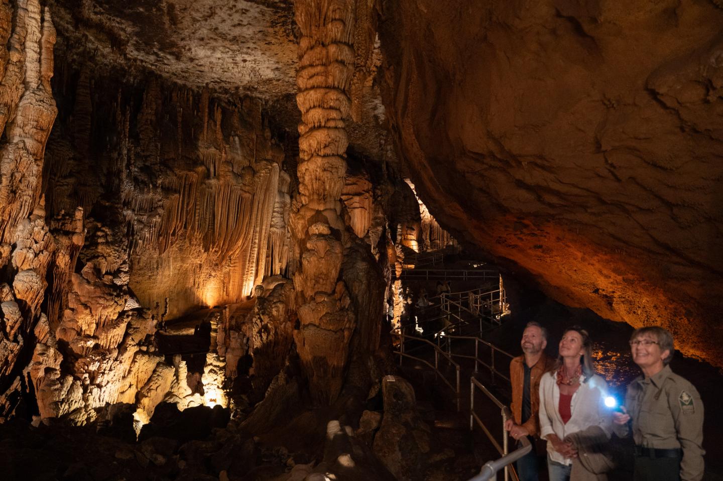 Tourists explore a dimly lit cave with stalactites and stalagmites.