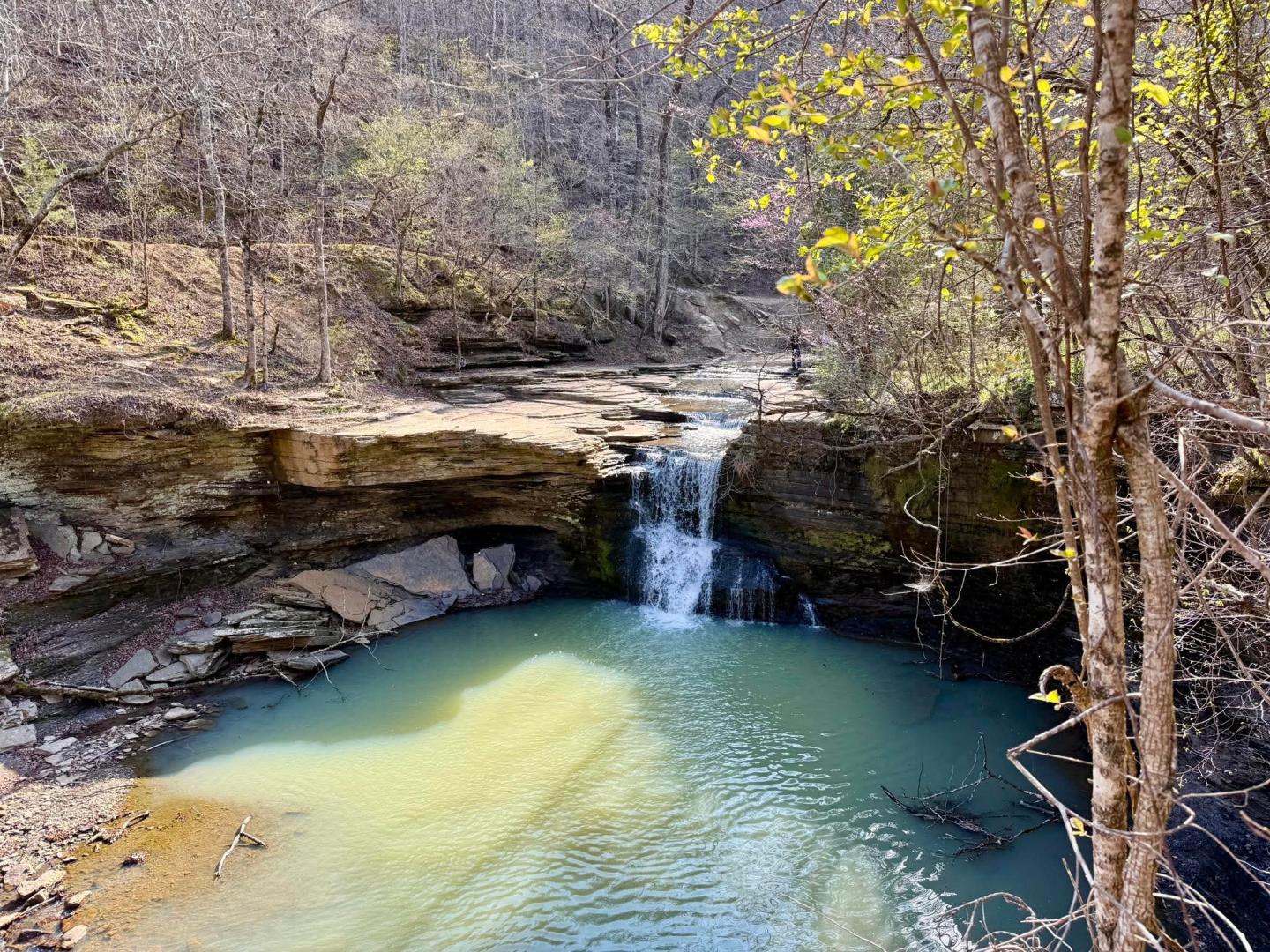 Waterfall cascading into a turquoise pool surrounded by rocky cliffs and trees.