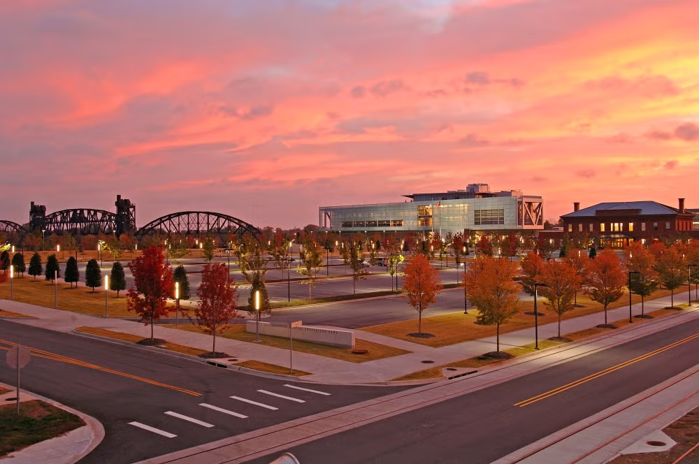 Sunset over a park with colorful autumn trees and a modern building.