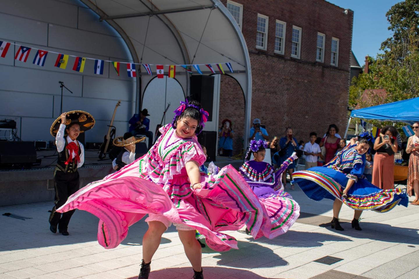 Dancers in colorful traditional dresses perform outdoors on a sunny day.