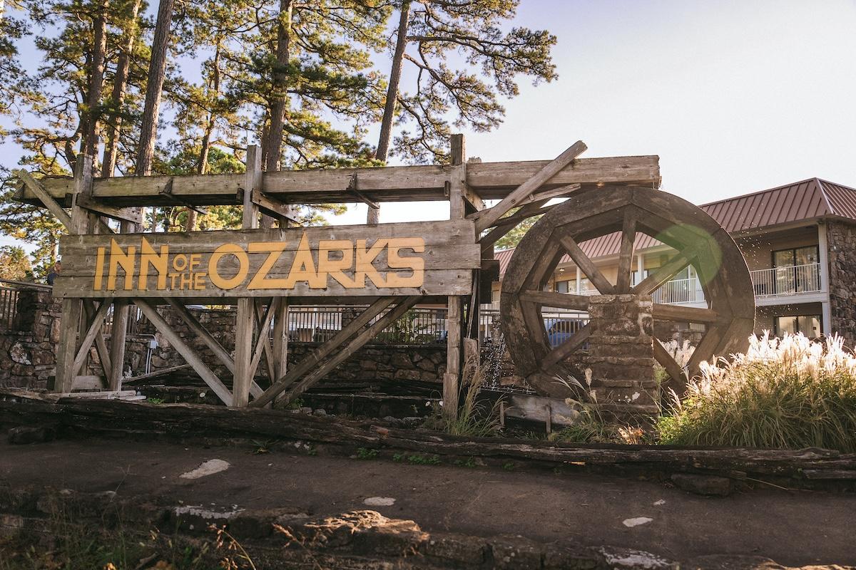 Wooden waterwheel next to an "Inn of the Ozarks" sign among trees.