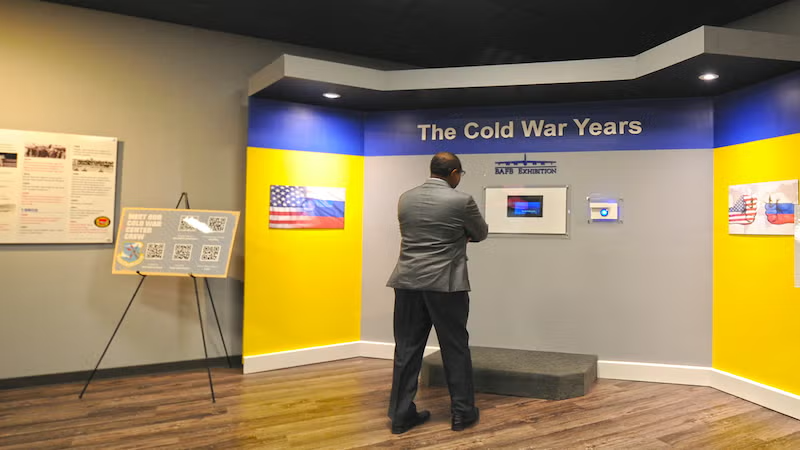 Man in suit examines Cold War exhibit in a museum setting.