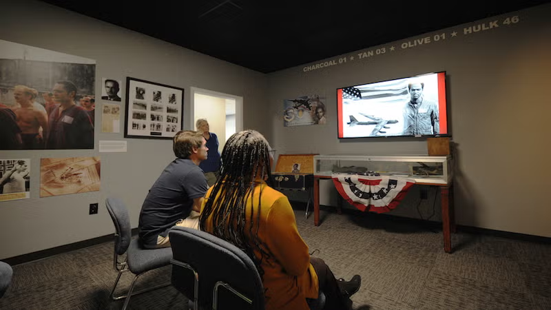 People watching a black and white video in a small museum room.