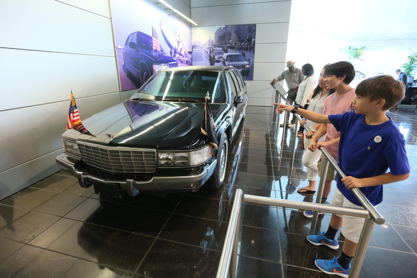 Black car on display in museum, with two kids pointing at it.
