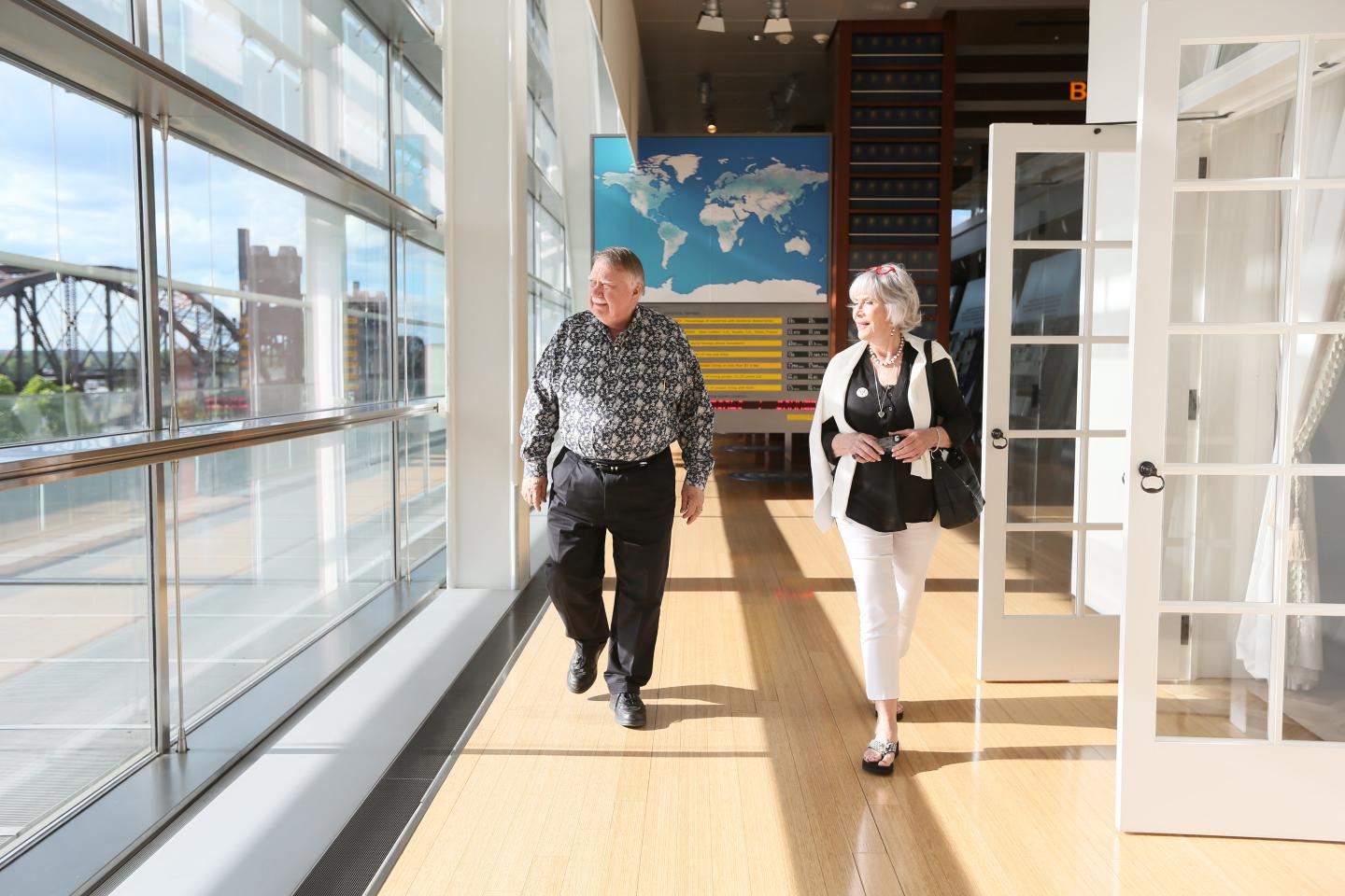 Two people walking in a sunlit hallway with a world map on the wall.