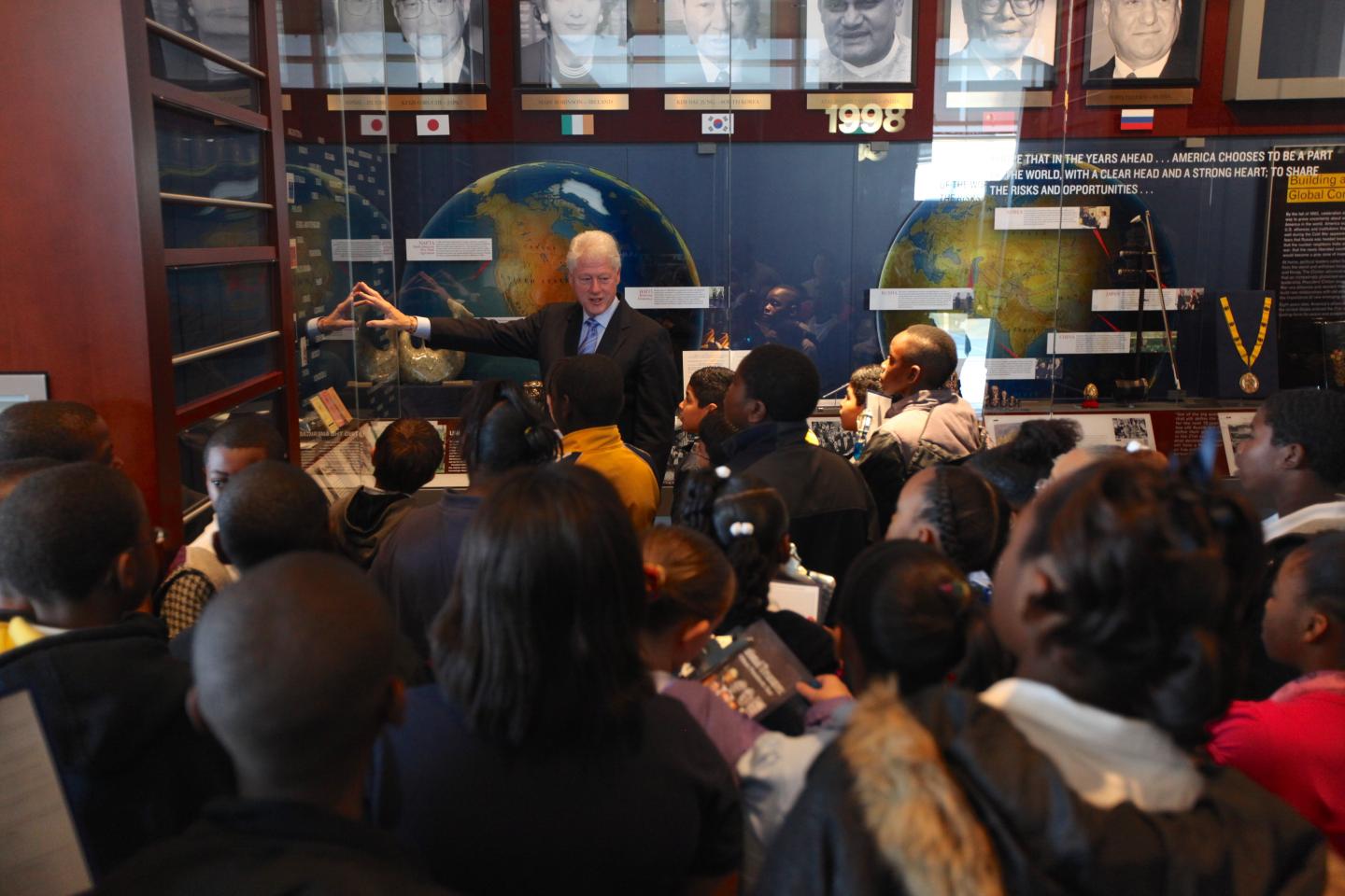A group of children listens to a speaker in a museum exhibit.